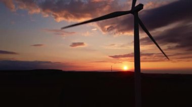 Gün batımında tarlada yel değirmeni türbini silueti. Dönen rüzgar jeneratörü