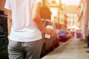 Kadın elinde kağıt kahve bardağıyla şehir caddesinde yürüyor.