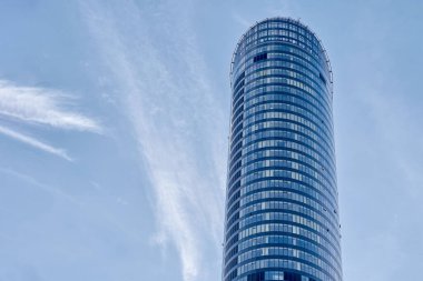 Kıvrımlı, uzun, cam gökdelenin alçak açılı görüntüsü. Mavi gökyüzüne karşı ofis binası. Çağdaş mimari tasarım