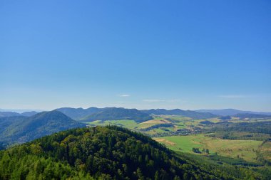 Wide panoramic view of green valley and forested mountain hills under blue summer sky. Beautiful natural landscape