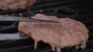 Mangalda metal maşayla pişirilmiş hamburgerin yakın çekimi. Yemek pişirme, et hazırlama, fast food ve açık hava yemekleri kavramı
