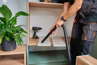 Matkap ve aletlerle mobilya montajı sırasında raflardan talaş süpüren biri. DIY ev geliştirme ve işten sonra temizlik