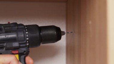 Mobilya montajı sırasında ahşap dolap panelinde elektrikli matkap delme deliği yakın görüntüsü