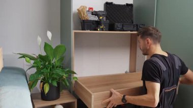 Adam evde ahşap dolap kuruyor. İşçiler gardıroba kendi yaptıkları çekmeceleri kuruyorlar. Dairenin yenilenmesi sırasında DIY mobilya montajı