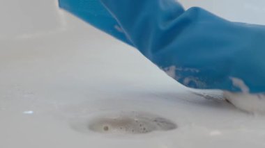 Modern banyoda beyaz küveti süngerle ve deterjanla temizleyen mavi lastik eldivenler giy. Ev hijyeni, temizlik ve günlük ev işleri kavramı