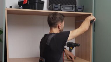 Evdeki mobilya montajı sırasında paneli işaretlemek için bant ve kalem kullanan adam ahşap dolabı ölçüyor.