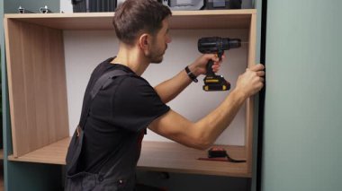 Tahta dolapta elektrikli matkapla delik açan bir adam. Dairenin yenilenmesi sırasında ev mobilyası montajı