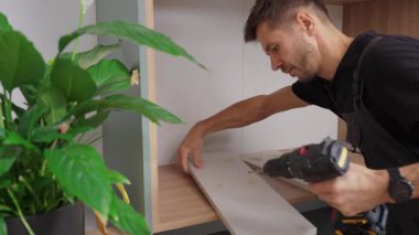 İşçi tahtada delik açmak için elektrikli matkap kullanıyor. Evdeki mobilyaları monte eden, rafları kendi elleriyle dolaba koymaya hazırlayan bir adam. Yenileme ve iç iyileştirme kavramı