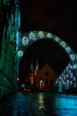 Renkli ışıklarla süslenmiş köprü ve aydınlatılmış katedral kuleleri. Gece Vaftizci Aziz John Katedrali