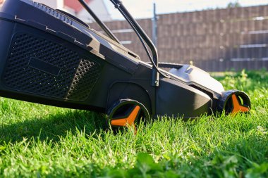 Elektrikli çim biçme makinesi banliyö evinin arka bahçesinde yeşil çim biçiyor. Bahçe işleri, peyzaj ve ev bakımı kavramı.