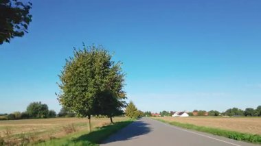 Güneşli bir günde kırsal yolda ağaçlar ve tarlalarla hareket eden birinci şahıs görüntüsü. Kırsal alanda araba sürme bakış açısı