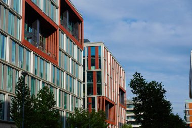 Şehir iş alanındaki ağaçlarla çevrili cam cepheli ve kırmızı dikey panelli çağdaş ofis binaları. Şehirde modern mimari ve kurumsal tasarım kavramı