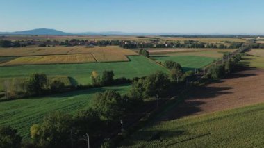 Tarım arazileri olan hava manzarası, demiryolu sınırı yakınlarındaki küçük köy ve açık mavi gökyüzünün altındaki dağ sıraları.