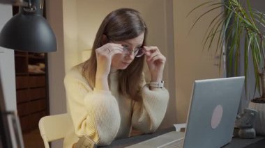 Masasında dizüstü bilgisayarla oturan, elinde bardaklarla gözlerini ovuşturan yorgun bir kadın. Yorgun insan geç saatlere kadar çalışıyor. Göz yorgunluğu, stres, baş ağrısı ve aşırı çalışma kavramı