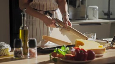 Önlüklü bir kadın güneş ışığı mutfağındaki tepsiye taze sebzeler, balkabağı, türler ve zeytinyağı koyuyor. Ev yemeği, hazırlık ve sağlıklı ev yemekleri kavramı