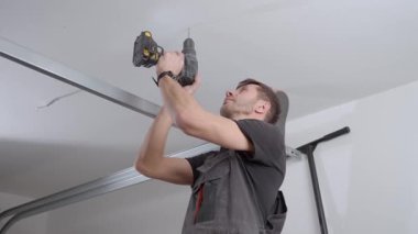İş tulumu giyen bir adam tavan arasında kablosuz matkapla delik açıyor. Ev yenileme, kurulum ve profesyonel bakım hizmeti kavramı.