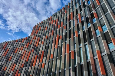 Günışığı altında dikey metal panelleri ve pencereleri olan çok renkli bir şehir binasının modern geometrik cephesi. Tekrarlayan geometrik şekillere sahip çağdaş şehir mimarisi.