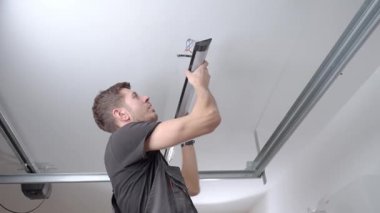 İçeriye tavan lambasını yerleştirirken elektrik kablolarını bağlayan iş elbisesi giyen bir adam. Işıklandırma, elektrik işi ve ev içi onarım kavramı