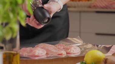 Ev mutfağında yemek hazırlarken çiğ tavuk filetosu biberli ve folyolu baharatlı kadın. Yemek pişirme, malzeme ve sağlıklı yemek kavramı..