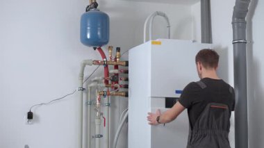 Teknisyen, içerideki ısı pompası sistemini borular ve genişleme tankıyla yüklüyor. Adam kontrol panelini ısı pompasına ayarlıyor. Ev ısıtma kurulumu, enerji verimliliği ve havalandırma bakımı kavramı