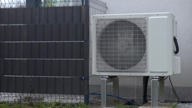 Koruyucu ızgaranın arkasında dönen vantilatörlü açık hava ısı pompası ünitesi. Yenilenebilir ısıtma, HVAC teknolojisi ve enerji tasarruflu iklim kontrol sistemi kavramı