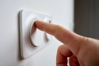 İç duvardaki modern beyaz ışık düğmesine, kapalı mekan ışıklarını açmak için yakın plan. Elektrik kullanımı, ev denetimi ve enerji tüketimi kavramı