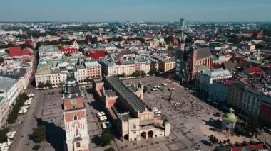 Güneşli bir günde renkli binaları çevreleyen yürüyen turistlerle tarihi Kumaş Salonu (Sukiennice) ile Krakow ana pazar meydanının hava manzarası.