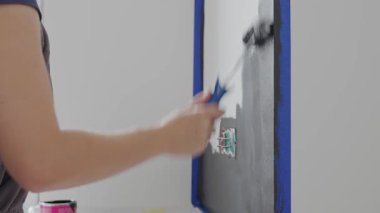 İç duvarı elektrik prizi ve maskeleme bandının yanında boya rulosuyla boyamış. Ev yenileme, iç yenileme, diy onarım ve duvar boyama işi kavramı.
