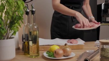 Eller mutfak tezgahına çiğ tavuk göğsü koyuyor yağ şişeleri ve sebzelerle. Ev yemeği, yemek hazırlama ve gıda malzemeleri kavramı.