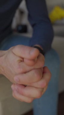 Evdeki kanepede oturan endişeli adamın sıkıca sarılmış elleri. Gergin insan sorun için endişeleniyor. Kaygı, depresyon, stres ve akıl sağlığı kavramı