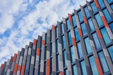 Gündüz gökyüzü altında dikey beton panelleri ve cam pencereleri olan çok renkli bir şehir binasının modern geometrik cephesi. Çağdaş şehir mimarisi
