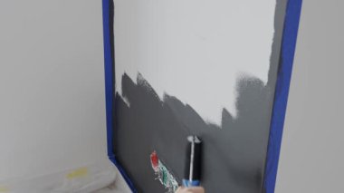 İç duvarı elektrik prizi ve maskeleme bandının yanında boya rulosuyla boyamış. Ev yenileme, iç yenileme, diy onarım ve duvar boyama işi kavramı.