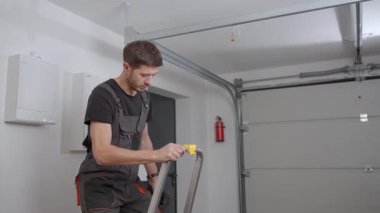 İş elbiseli bir adam elinde matkapla merdivene tırmanıyor ve içeride tavanı delmeye hazırlanıyor. Elektrik tesisatı, yenileme ve profesyonel bakım kavramı.