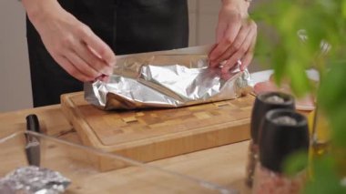 Kadın eli, baharatlı çiğ tavuk göğsünü alüminyum folyoyla mutfakta tahta kesme tahtasına sarıyordu. Yemek hazırlama ve pişirme süreci kavramı