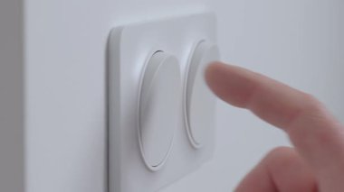 İç duvardaki modern beyaz ışık düğmesine, kapalı mekan ışıklarını açmak için yakın plan. Elektrik kullanımı, ev denetimi ve enerji tüketimi kavramı