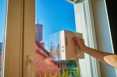 Kadın pencerenin cam yüzeyinde robot pencere temizleyicisine başlıyor. Evdeki pencere temizliği için otomatik aygıt kullanılıyor. Akıllı ev aletleri kavramı