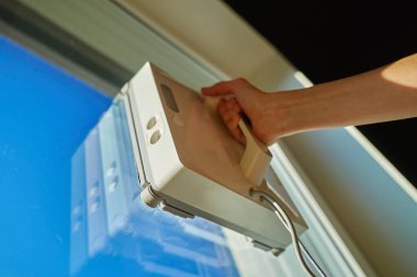 Kadın pencerenin cam yüzeyinde robot pencere temizleyicisine başlıyor. Evdeki pencere temizliği için otomatik aygıt kullanılıyor. Akıllı ev aletleri kavramı