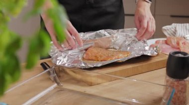 Kadın eli, baharatlı çiğ tavuk göğsünü alüminyum folyoyla mutfakta tahta kesme tahtasına sarıyordu. Yemek hazırlama ve pişirme süreci kavramı