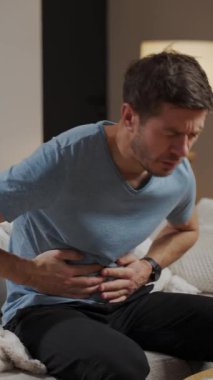 Oturma odasında koltukta oturan bir adam karın ağrısı ve kramplardan muzdarip. Sağlık sorunları olan kişi, sindirim sorunları veya evde gıda zehirlenmesi