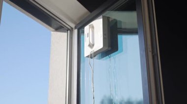 Kare cam temizleme robotu cam yıkıyor. Robotik pencere temizleyicisi mavi gökyüzüne karşı pencere yüzeyinde çalışıyor. Akıllı ev aletleri kavramı