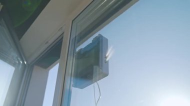 Kare cam temizleme robotu cam yıkıyor. Robotik pencere temizleyicisi mavi gökyüzüne karşı pencere yüzeyinde çalışıyor. Akıllı ev aletleri kavramı