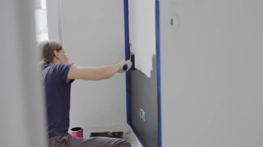 Ev tadilatı sırasında, beyaz iç duvarı siyah renge boyayan bir kadın ve oturma odasında boya silindiri. DIY geliştirme ve apartman yenileme kavramı