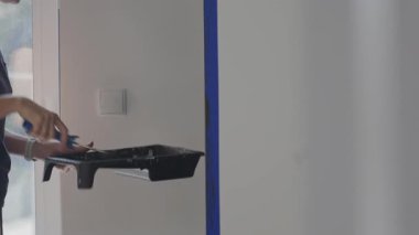 Duvarın iç tarafına siyah boya sürmek için boya rulosu kullanan ve kenar boyunca bant yapıştıran birinin yakın çekimi. Ev yenileme, duvar onarımı ve apartman onarımı kavramı
