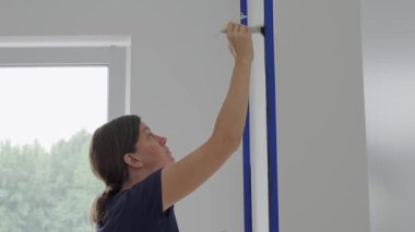Modern odadaki pencerenin yanında kadın iç duvarı fırçayla boyuyor. Ev yenileme, iç boyama ve DIY onarım kavramı.