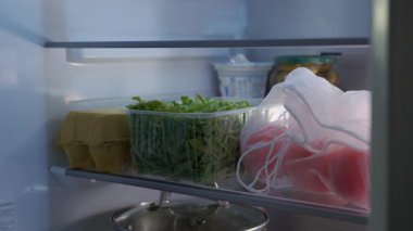 Buzdolabını açarken ellerinizi kapatın ve taze yeşil roka yapraklı domates ve plastik kabı alın. Sağlıklı beslenme, ev yemeği depolama ve yemek hazırlama kavramı