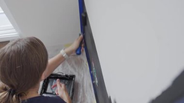 Ev tadilatı sırasında, beyaz iç duvarı siyah renge boyayan bir kadın ve oturma odasında boya silindiri. DIY geliştirme ve apartman yenileme kavramı