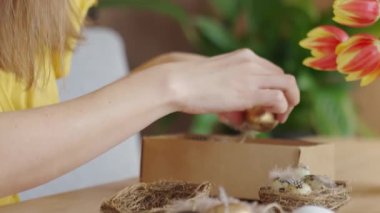 Süslü, altın Paskalya yumurtası süsü taşıyan bir kadın. Tüylü ve ipli siyah beyaz yumurta ve yuvalı ahşap masa.