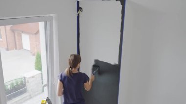 Ev tadilatı sırasında, beyaz iç duvarı siyah renge boyayan bir kadın ve oturma odasında boya silindiri. DIY geliştirme ve apartman yenileme kavramı