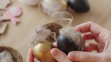Tüylerle süslenmiş el yapımı Paskalya yumurtalarını tut. DIY tatil dekorasyonu ve bahar sanatı hazırlığı kavramı.
