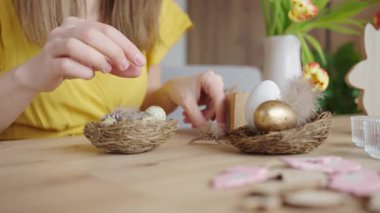 Küçük yumurta ve tüyleri, laleler ve Paskalya dekoruyla ahşap masaya yerleştiren bir kadın. Bahar tatili hazırlığı ve el yapımı dekorasyon kavramı